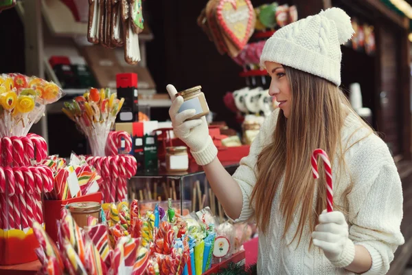 Street portrait of beautiful young woman choosing some sweets on the festive Christmas fair. Lady wearing classic stylish winter knitted clothes. Close up