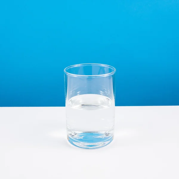 Half empty or half full glass of water on white table.