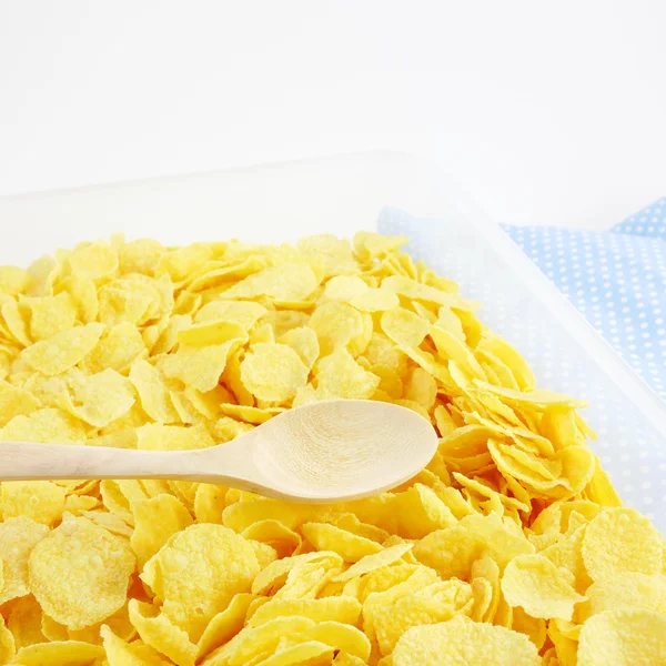 The tasty golden corn flakes and wooden spoon in plastic container box