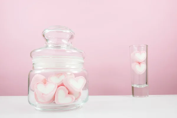 The lovely pink heart marshmallows in small glass jar and small narrow glass on white table for Valentine\'s day.