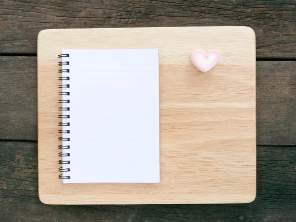 The white note book and lovely pink heart marshmallow and wooden board