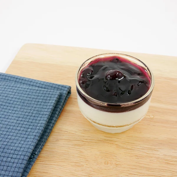 The tasty homemade blueberry panna cotta (Italian pudding dessert) in the small glass and blue cotton fabric