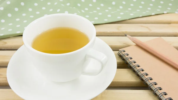 The cup of Japanese green tea and green cotton fabric on wooden tray.