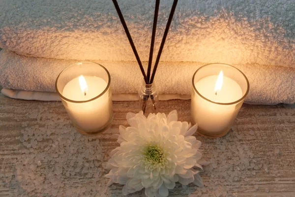 Spa composition with white towels, candles, flowers, incense sticks and bath salt on wooden table