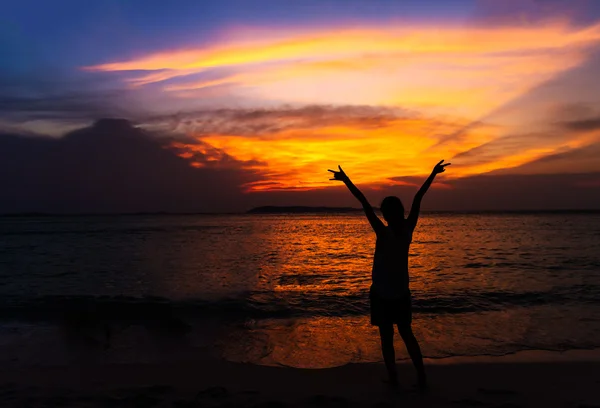 Silhouette of young woman spreading hand and relaxing on the beach at sunset.