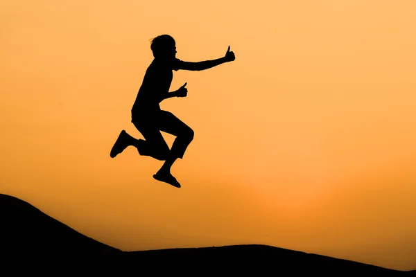 Silhouette of man in happy jumping and thump up on orange sunset sky