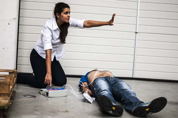 Girl assisting an unconscious man with defibrillator and CPR