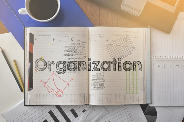 Notebook with text inside Organization on table with coffee and some papers around