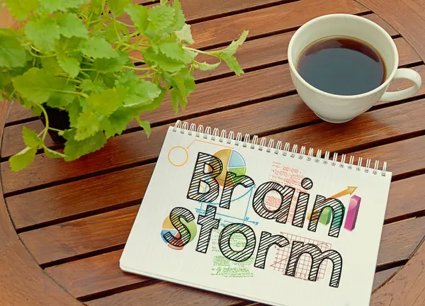 Notebook with text inside Brainstorm on table with coffee and plant