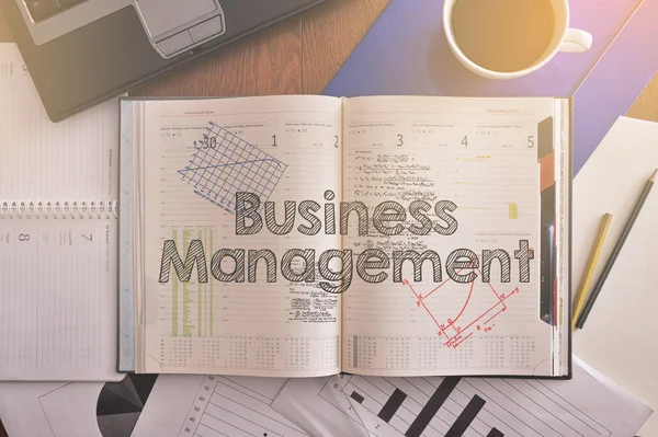 Notebook with text inside Business Management on table with coffee and some diagrams