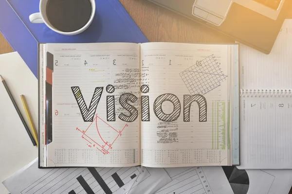 Notebook with text inside Vision on table with coffee and some diagrams