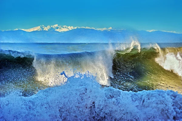 High stormy waves and snow-capped mountains the background
