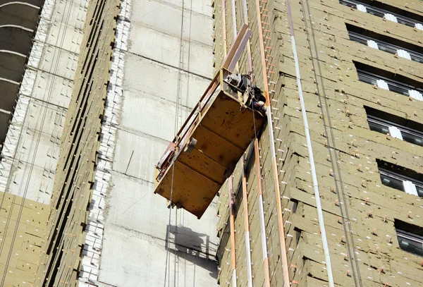 Construction suspended yellow cradle with workers on a newly built high-rise building