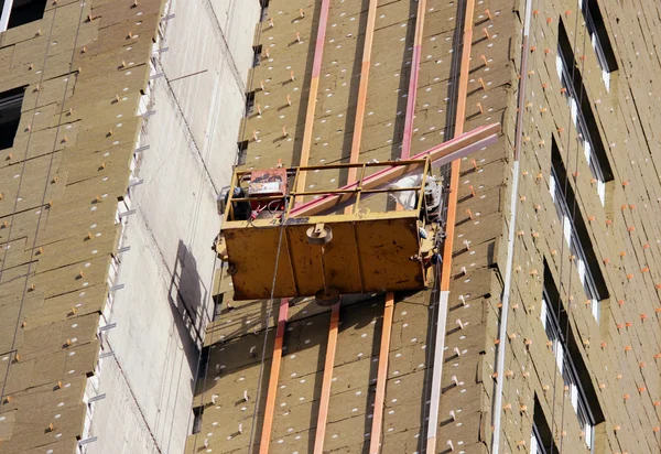 Construction suspended yellow cradle with workers on a newly built high-rise building