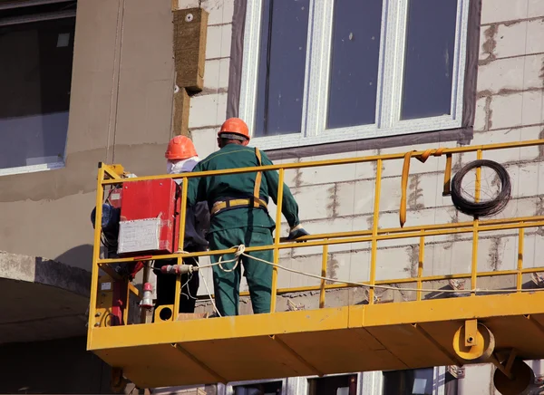 Construction suspended yellow cradle with workers on a newly built high-rise building