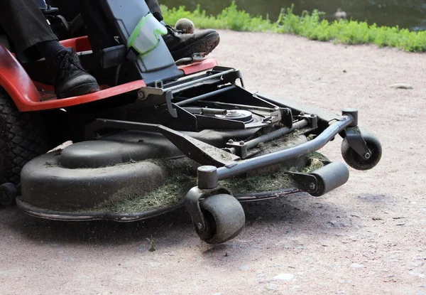 Worker of park rides on the mower  gravel road.