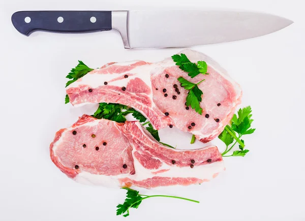Two juicy piece of meat on the bone with a  pepper and knife  lie on White background