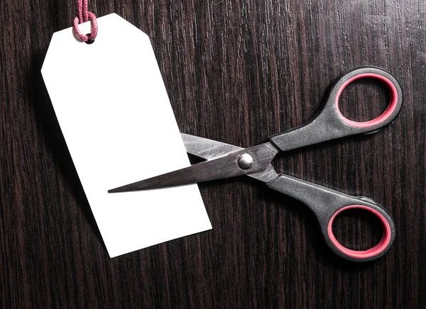 Scissors cut paper white price tag on a brown wooden background. Stock. Discounts. Benefit. marketing concept