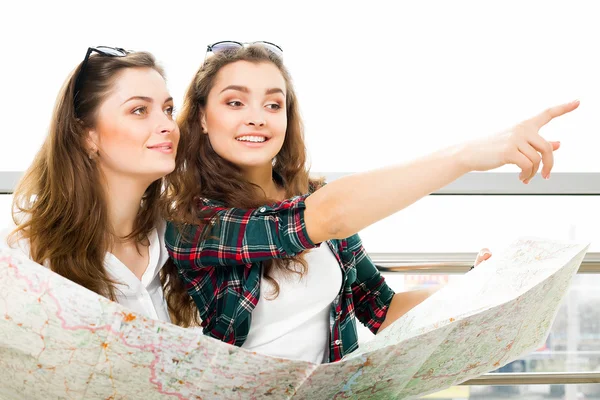 Two young dark-haired girl looking at the map and show the direction of the index finger