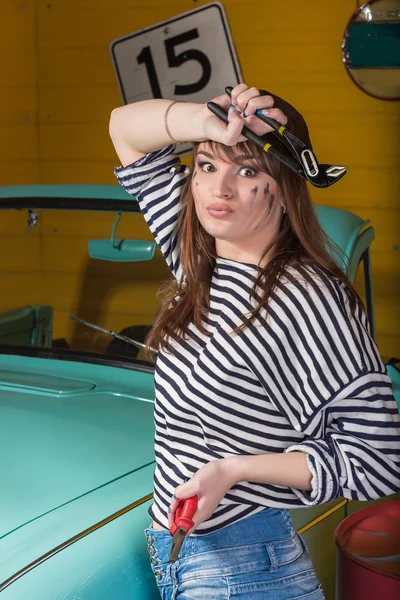 Attractive  brunette woman in a striped jacket in the garage near the retro car, in the hands holding tools.