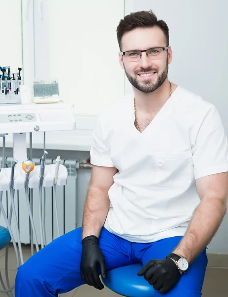 Healthcare, profession, stomatology and medicine concept - smiling male young dentist over medical office background