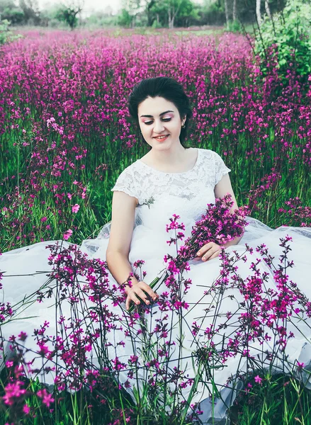 Beautiful bride in a flower field. The girl in a white dress with a bouquet in a summer field at sunset