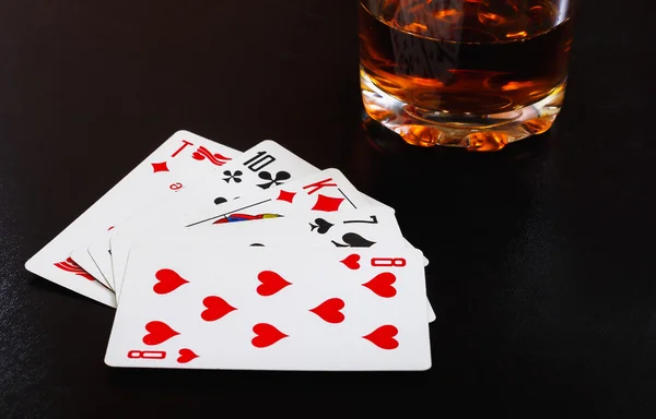 Glass of whiskey and playing cards on a black desk on the wooden table. Angle view, identification cards