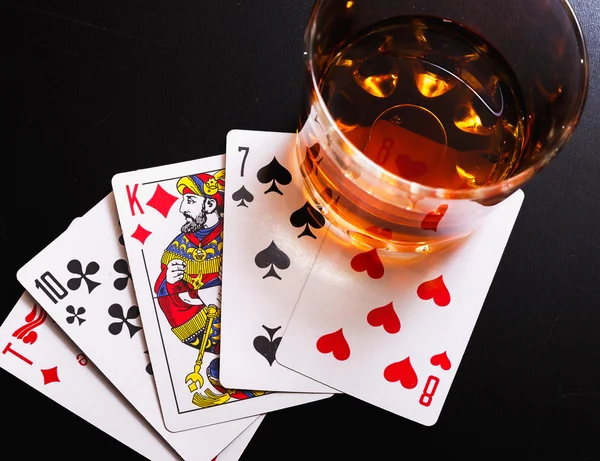 Glass of whiskey and playing cards on a black desk on the wooden table. Angle view, identification cards