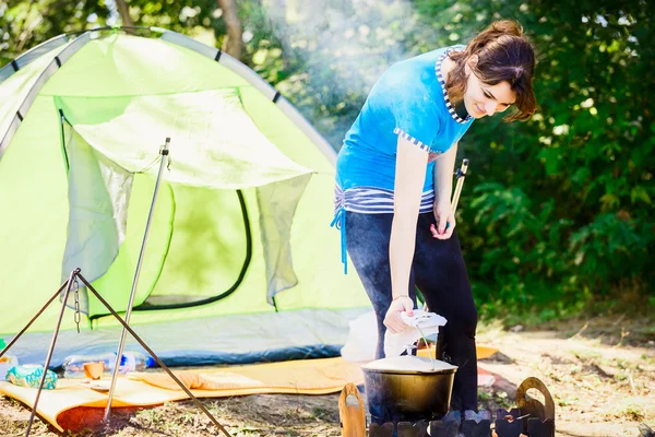 Young woman tourist near a tent in the woods preparing food over a fire.tourism concept