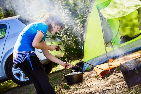 Young woman tourist near a tent in the woods preparing food over a fire.tourism concept