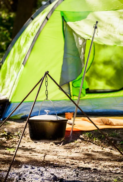 A pot hanging on a tripod on the background of the tent. Cooking over a campfire on the nature