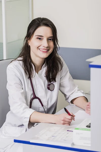 Girl Doctor in a white coat sitting at a desk with a pen