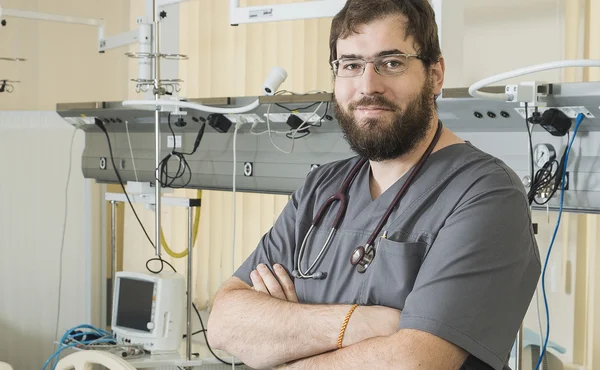 Bearded doctor wearing glasses and a gray robe works with hospital equipment