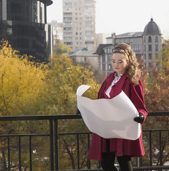 Smiling businesswoman studying the sketch of future business centre. Attractive lady in business suit is satisfied by the plan made by architect.