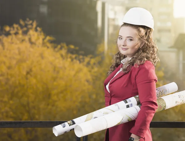 Smiling businesswoman in helmet studying the sketch of future business centre. Attractive lady in business suit is satisfied by the plan made by architect.