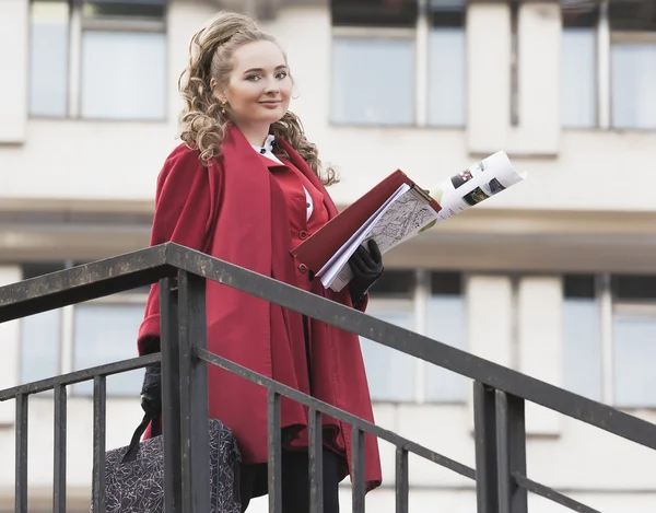 Young beautiful woman architect in red jacket standing near the railing with the drawings lestnitsy.Student