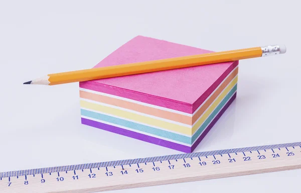 A wooden ruler lying on a pack of colored paper on a white table