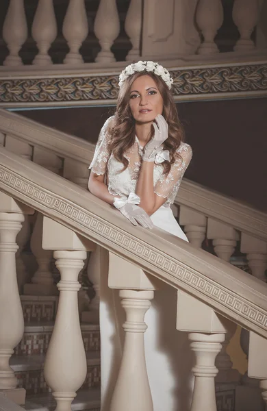 Beautiful elegant girl in a white dress standing on vintage stairs in the castle