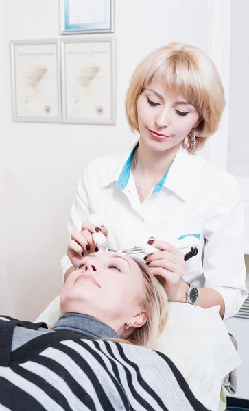 Beautiful girl beautician making permanent makeup on woman\'s face. Blonde. doctor.