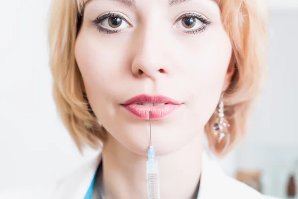 Beautiful young beautician standing in his office in a white robe and holding a needle in the syringe near the lips.woman doctor.