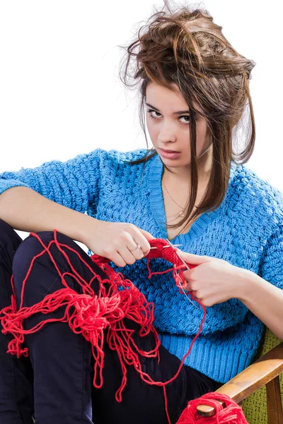 Tortured young girl in a  sweater sits on a chair with a red ball of yarn and knitting a scarf and Spitz. Tired. White background.