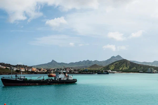 Ship in front of small town at the blue ocean coast with cloudy mountain background, Cape Verde island