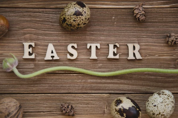 Easter letter on wooden background decorated with nuts, flowers and eggs