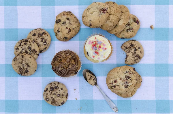 Tasty cookies and muffins cakes with chocolate cream decorated with sugar candies on a blue checkered tablecloth