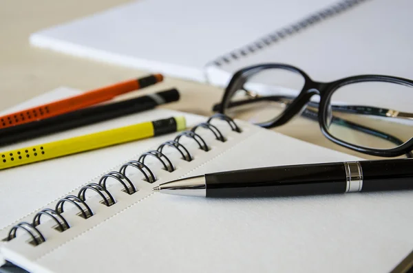 Representative pen laying on a blank note book with pencils and glasses  on table. Tilt-up  close-up view