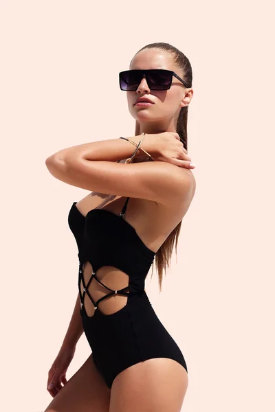 Woman in black sunglasses and swimsuit wearing golden bracelet with hair up poses on isolated white background. Fashion tan model. Beautiful awesome cool girl. Phuket island, Thailand.