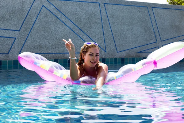 Woman wearing sunglasses and bikini poses swimming on mattress in pool. Phuket island, Thailand