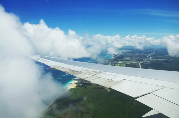 Wing of an airplane flying above the clouds over tropical island