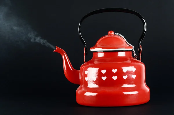 Red kettle isolated on black. Steam coming out.