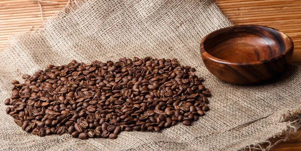 Brown coffee beans on the bag with empty wooden dish and bamboo background